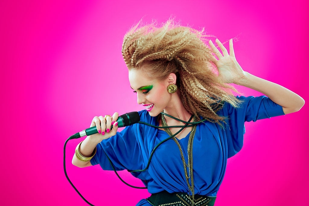 Portrait of 1980s style happy young woman dancing and singing into microphone. - Latest Fashion & Lifestyle Trends 80s hairstyles