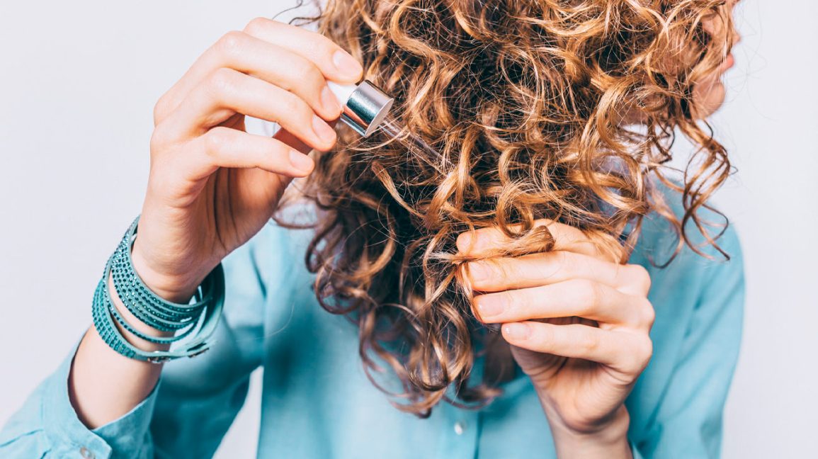 Young-woman-in-blue-shirt-holding-her-curly-hair-tips-1296x728-header-1296x728 - Latest Fashion & Lifestyle Trends tips to fix frizzy hair